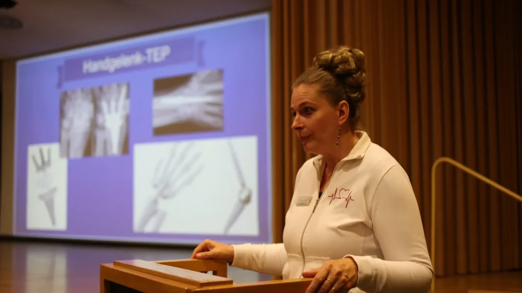 Eine Frau Ärztin hält einen Vortrag, im Hintergrund ist eine Projektion von medizinischen Bildern zu sehen, die an einer Wand präsentiert werden.