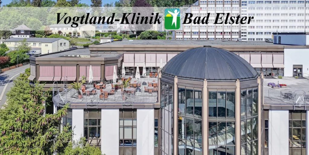 Dieses hochwertige Foto präsentiert die Vogtland-Klinik in Bad Elster, ein modernes Klinikgebäude, das harmonisch in eine bewaldete, hügelige Landschaft eingebettet ist und eine Atmosphäre von medizinischer Professionalität und Ruhe ausstrahlt. Die Komposition des Bildes ist horizontal ausgerichtet und zentralisiert das architektonisch markante Gebäude der Klinik. Im oberen Bereich ist der Schriftzug „Vogtland-Klinik Bad Elster“ inklusive Logo vor einem blauen Balken platziert. Das Hauptgebäude besteht aus einem weitläufigen, mehrstöckigen Komplex mit einer Kombination aus funktionalen weißen Fassaden, großen Fensterfronten und einer markanten, gläsernen Rotunde mit dunkler Kuppel im Vordergrund. Eine Außenterrasse mit Sonnenschirmen und Pflanzen belebt den vorderen Gebäudeteil, während der Hintergrund von einem dichten, grünen Waldhang dominiert wird, der dem gesamten Komplex eine natürliche Kulisse verleiht. Das Hauptobjekt ist das Gebäudeensemble der Vogtland-Klinik, das sich durch seine funktionale, jedoch architektonisch ansprechende Gestaltung auszeichnet. Die Struktur integriert unterschiedliche Elemente: den terrassenförmigen, langgestreckten Haupttrakt mit seinen zahlreichen Fensterreihen, den gläsernen Eingangsbereich mit der charakteristischen Kuppelkonstruktion und die großzügigen Außenflächen. Die weißen Fassadenflächen bilden einen deutlichen Kontrast zu den metallischen Fensterrahmen und der dunklen Dachgestaltung. Bäume und Büsche im Vorder- und Seitenbereich lockern das Erscheinungsbild auf und wirken einladend und gepflegt. Das Bild ist ein professionell aufgenommenes Architekturfoto mit hoher Detailgenauigkeit und einer klaren, natürlichen Farbwiedergabe. Die technische Ausführung zeichnet sich durch eine gleichmäßige Schärfentiefe aus, die sowohl die architektonischen Details des Gebäudes als auch die Textur der umliegenden Bäume präzise wiedergibt. Der Bildstil ist sachlich und dokumentarisch, typisch für eine Präsentation von Gesundheitseinrichtungen, wobei die Perspektive leicht erhöht gewählt wurde, um einen optimalen Überblick über die gesamte Anlage und deren Einbettung in die Umgebung zu gewährleisten. Die Umgebung ist durch ein sonniges, sommerliches Tageslicht geprägt, das das Gebäude gleichmäßig ausleuchtet und helle, klare Kontraste erzeugt. Das helle Licht betont die architektonischen Linien und lässt die weißen Fassaden strahlen. Der grüne Laubwald im Hintergrund sowie die Bepflanzung vor dem Gebäude vermitteln eine ruhige, gesundheitsfördernde Atmosphäre. Insgesamt erzeugt die Szene eine Stimmung von Beständigkeit, Ordnung und Wohlbefinden, die ideal zu der Funktion einer Rehabilitationsklinik passt, wobei das sonnige Wetter die positive und heilende Ausstrahlung des Standortes in Bad Elster unterstreicht.