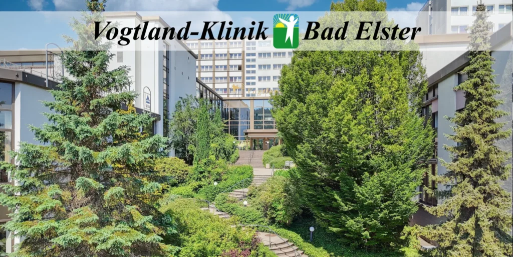 Das Bild zeigt die Vogtland-Klinik in Bad Elster, ein modernes Klinikgebäude, das harmonisch von einer weitläufigen, grünen Gartenanlage mit hohen Nadelbäumen und einem geschwungenen Treppenaufgang umgeben ist. Die Komposition ist frontal und symmetrisch ausgerichtet, wobei der zentrale Weg die Aufmerksamkeit des Betrachters direkt zum Haupteingang des Klinikkomplexes lenkt. Der Vordergrund wird von üppigem Grün und prägnanten Fichten dominiert, die den Raum einrahmen, während der Mittelgrund den Zugangsweg mit seinen geschwungenen Stufen zeigt. Im Hintergrund erhebt sich der eigentliche Gebäudekomplex, der durch seine klare architektonische Struktur und großflächige Verglasung besticht, was eine einladende und professionelle Atmosphäre schafft.